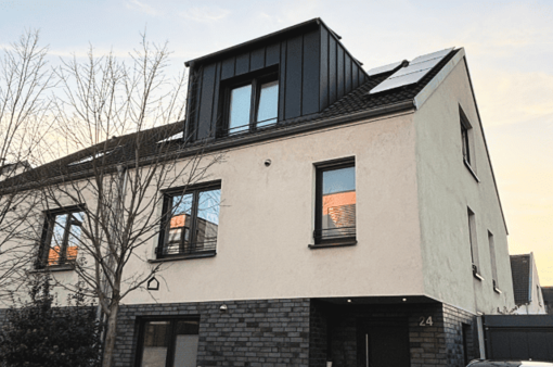 Nachher: Haus mit moderner Gaube Moderne Wohnhausfassade mit großen Fenstern und mit einer modernen Gaube. Bäume im Vordergrund. Wolkiger Himmel.